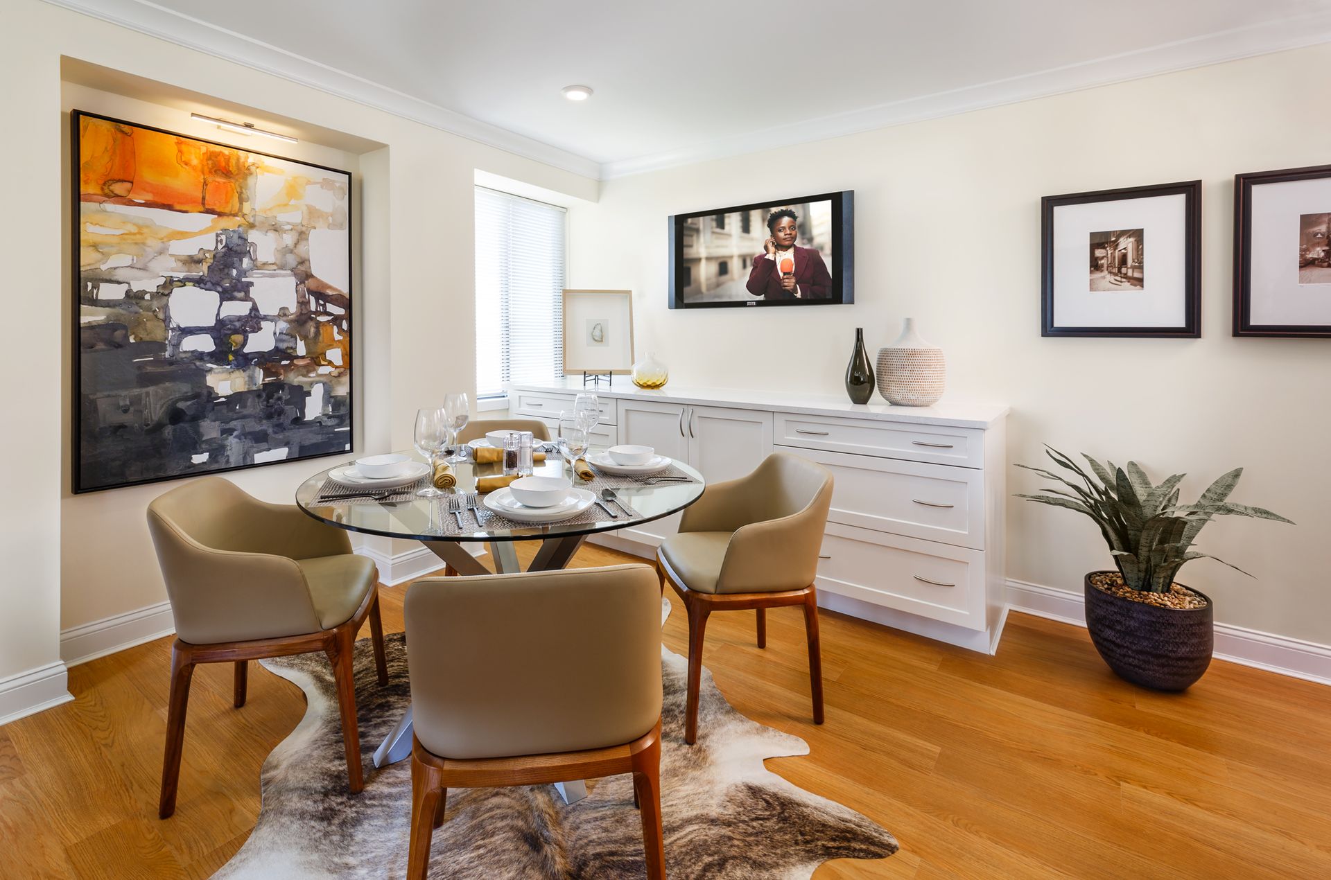 Bright dining room with glass table, tan chairs, white sideboard, wall art, and hardwood floors.