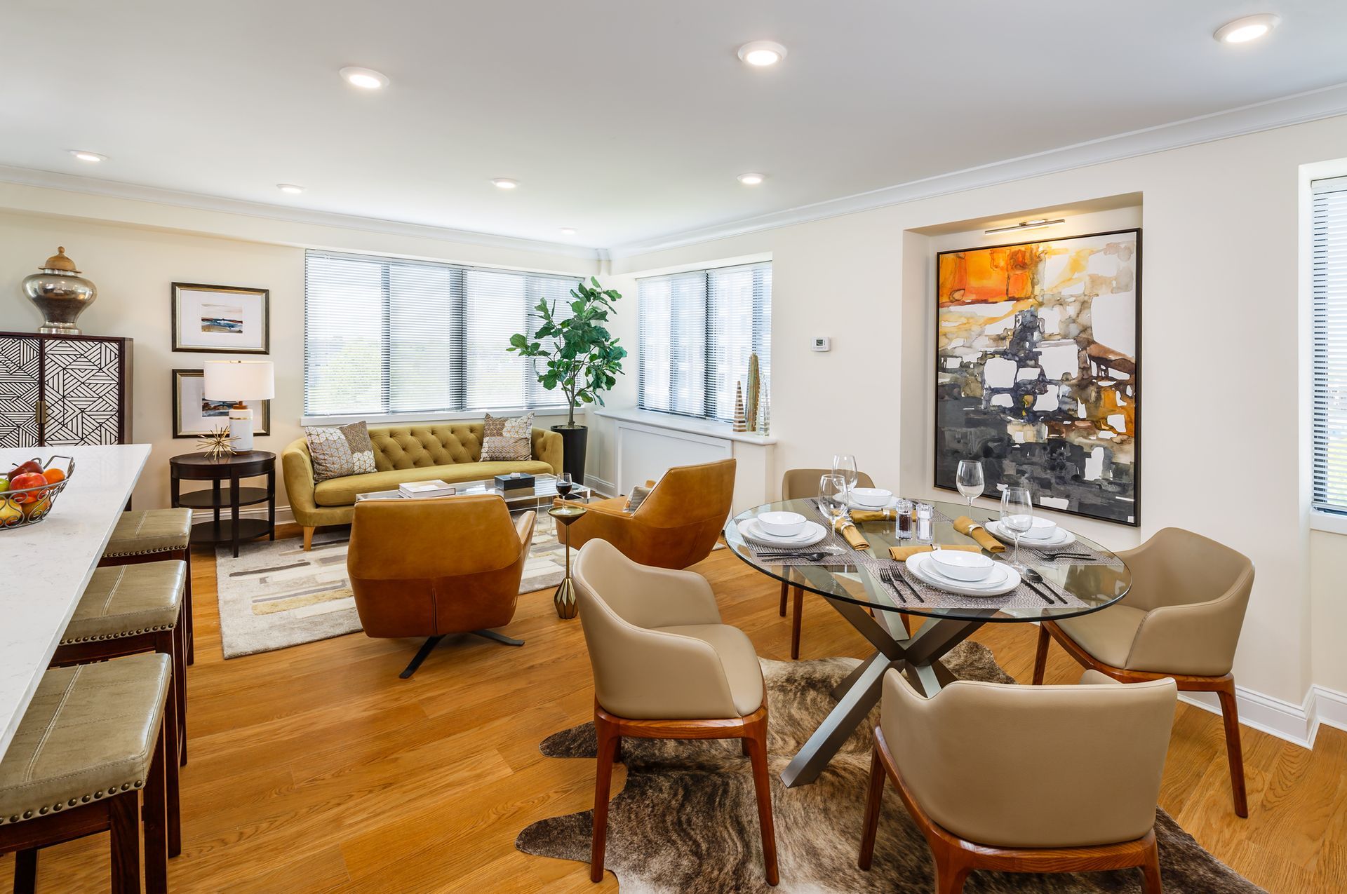 Bright modern living room with tan chairs, glass dining table, hardwood floors, and large windows.