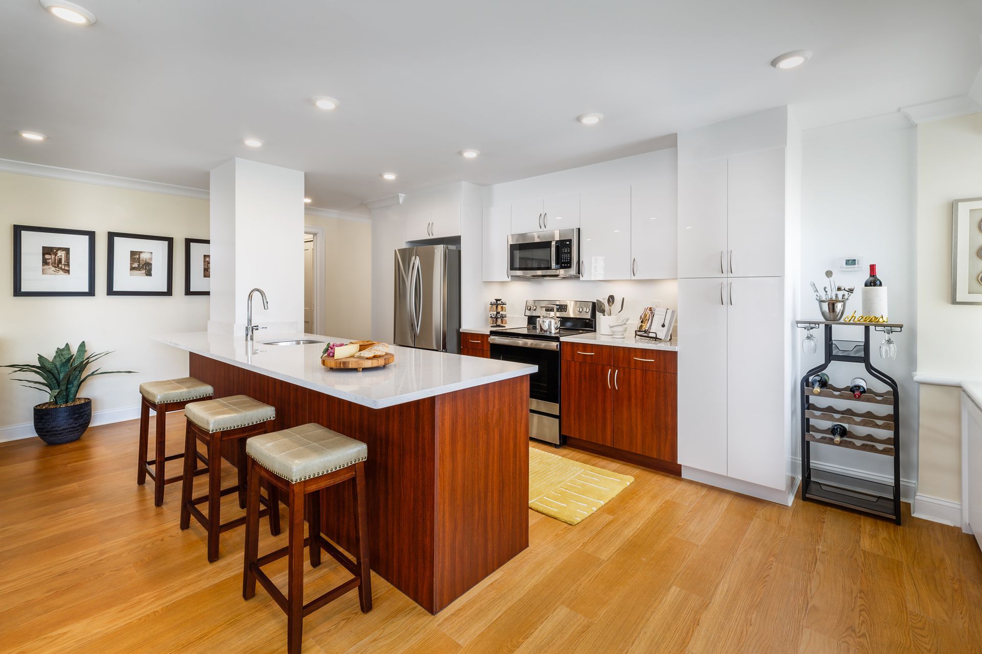 Bright modern kitchen with island, wooden stools, stainless appliances, and light wood floors.