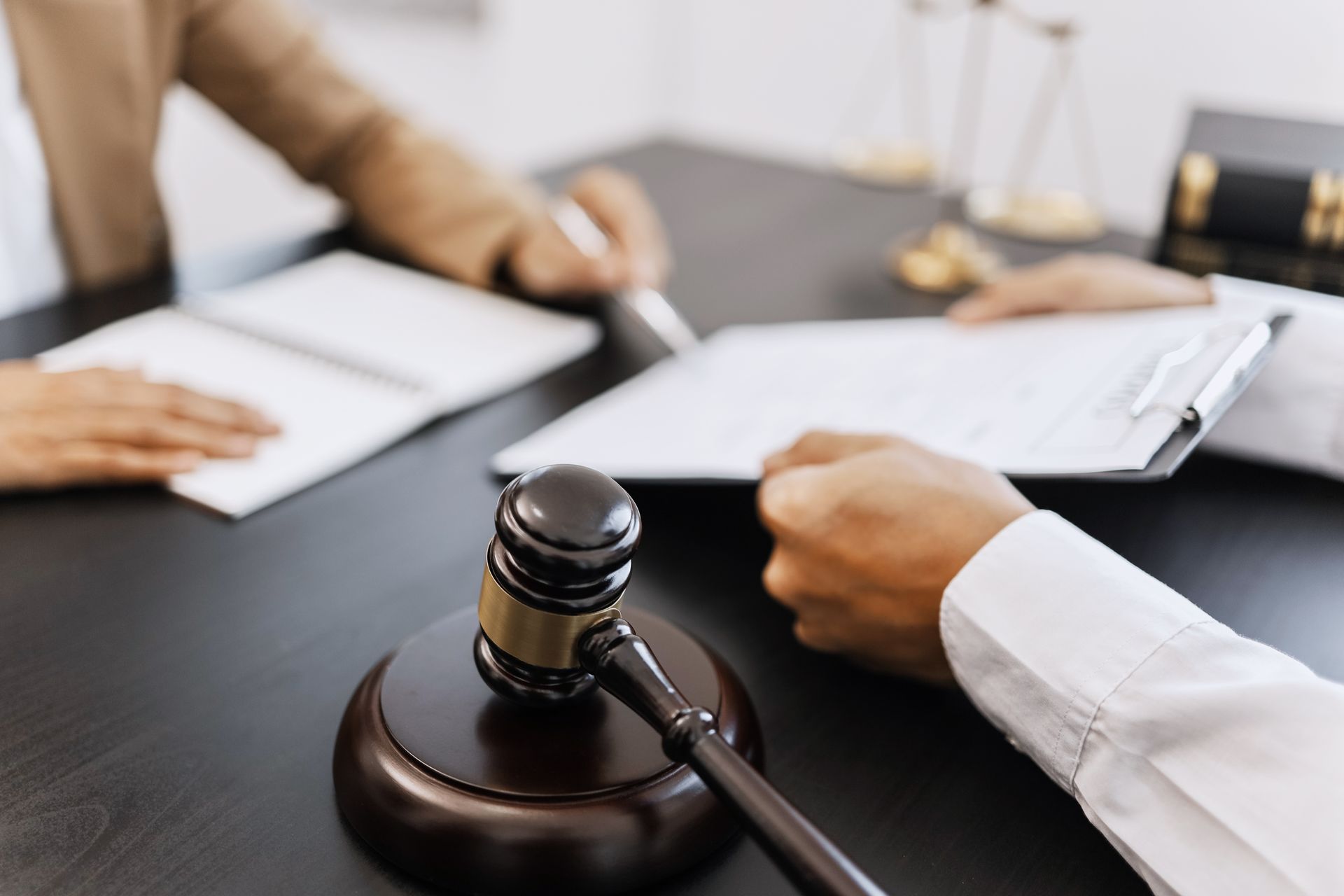 Cropped view of a lawyer preparing a document for his client to sign and a wooden gavel on his desk.