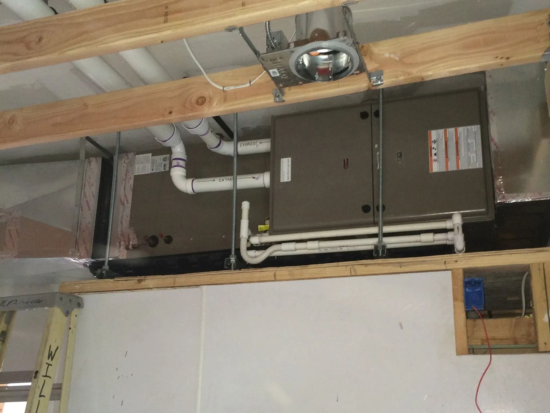 HVAC system installed in a ceiling. Two brown units with white pipes and ductwork, mounted with wooden supports.