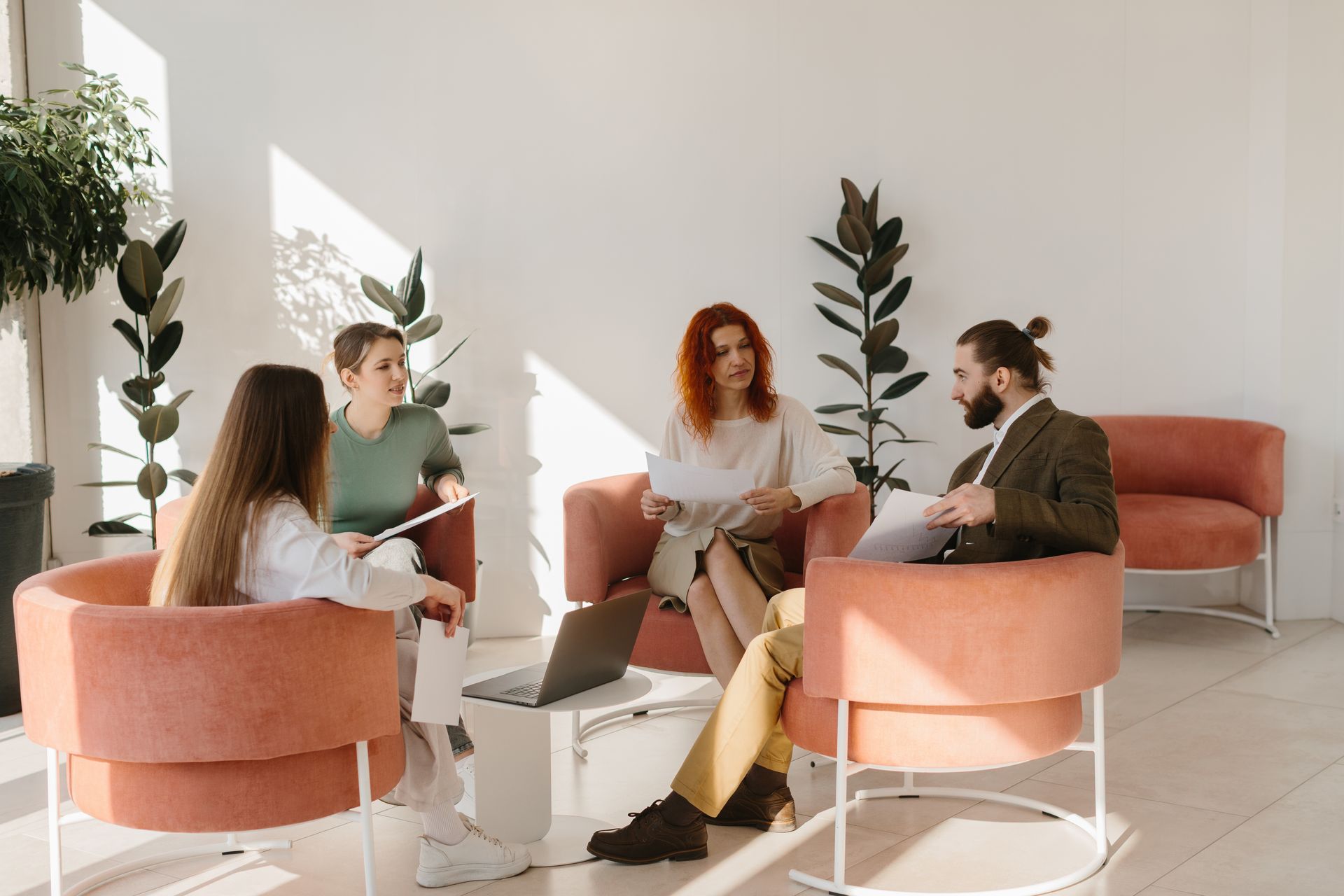 People meeting in a bright lounge with pink chairs and a laptop on a low table