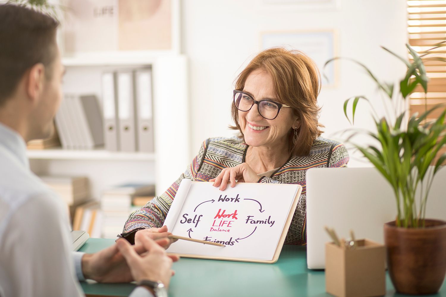 Woman smiling at a desk with a laptop and whiteboard in a bright office meeting Woman smiling at a desk with a laptop and whiteboard in a bright office meeting