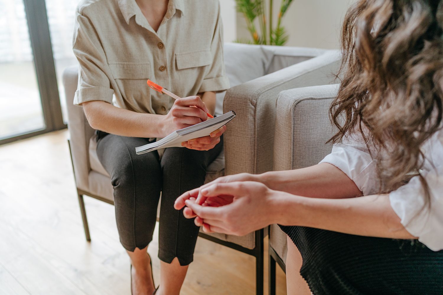 Two people in a counseling session, one taking notes on a clipboard beside a sofa. Two people in a counseling session, one taking notes on a clipboard beside a sofa.