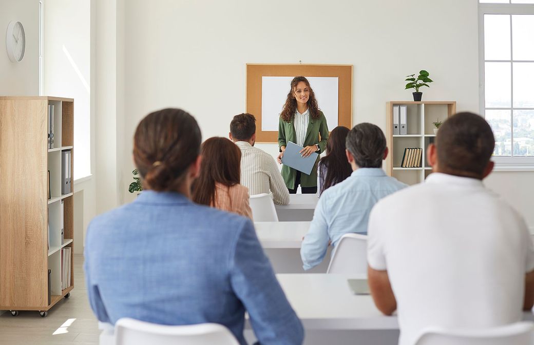 Small classroom presentation with a speaker at the front and seated audience members facing a screen Small classroom presentation with a speaker at the front and seated audience members facing a screen