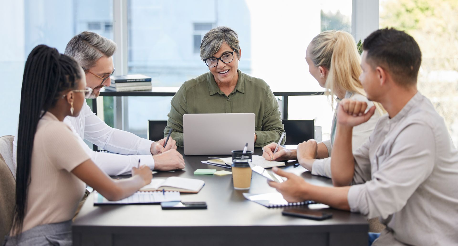 Team in a meeting around a laptop in a bright office, discussing work around a conference table