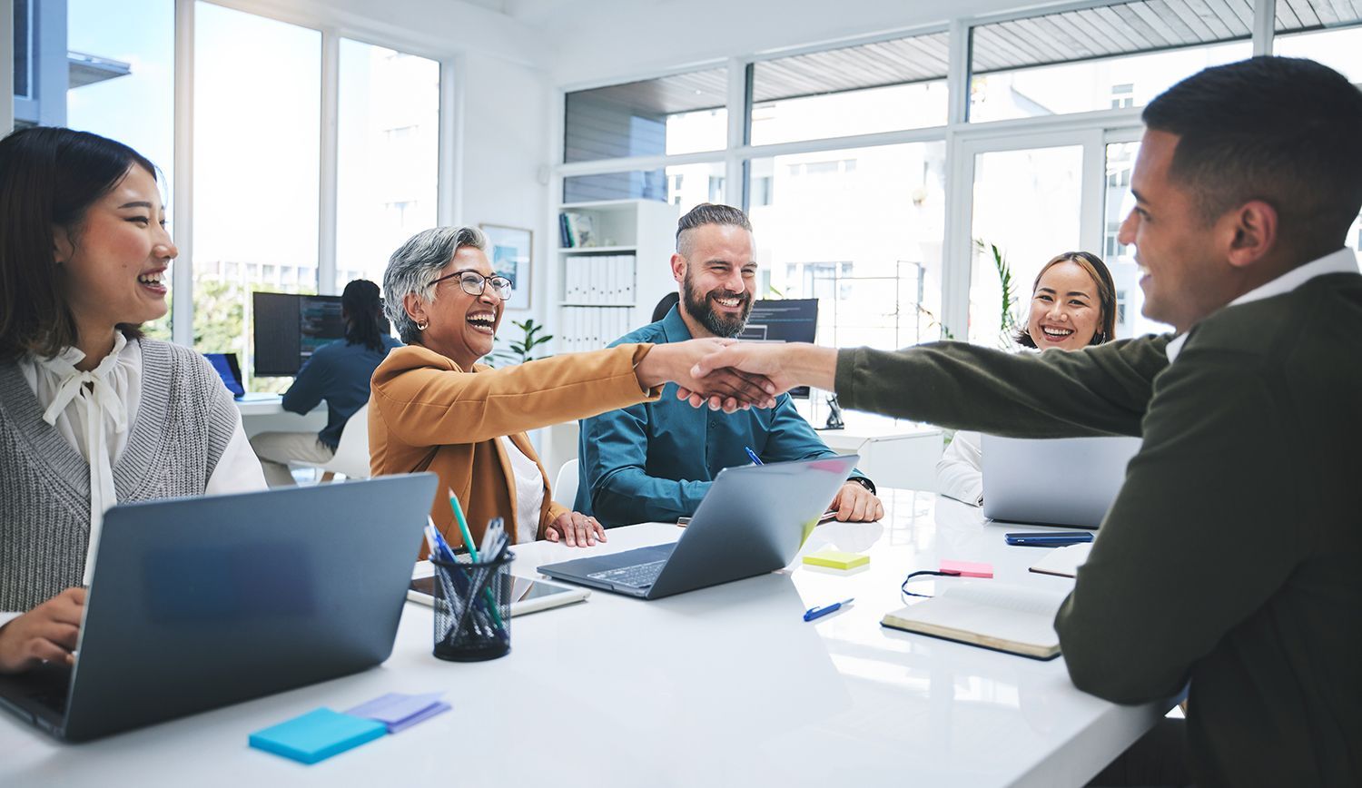 Team of coworkers in a bright office reaching across a table in a friendly handshake