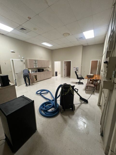 A person is working in a room with a vacuum cleaner. Cabinets and furniture are present.