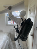 Person in protective suit inspecting a window, backpack vacuum visible.