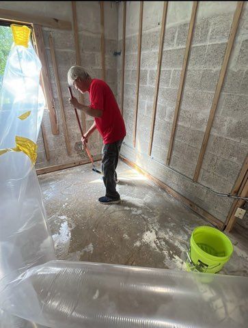 Man in red shirt sweeps wet floor in a room under construction with plastic sheeting.