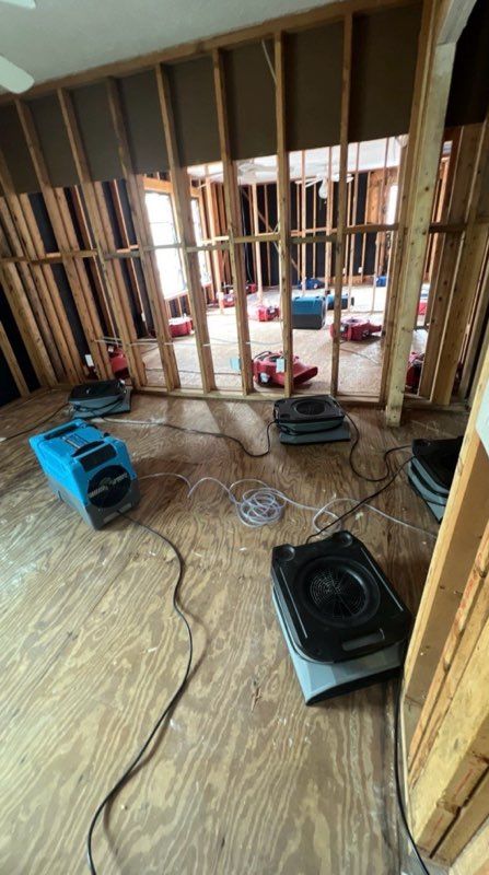 Dehumidifiers set up in a room with exposed wooden studs. Flooring is partially plywood.