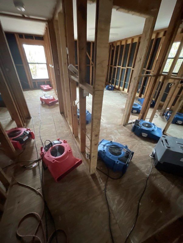 Interior with exposed framing, several air movers drying the room after water damage.
