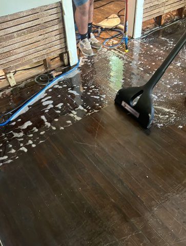 Flooded wood floor being cleaned with a squeegee. A person stands in the background.