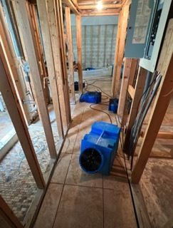 A hallway under construction with wooden studs. Blue dehumidifiers on the floor.