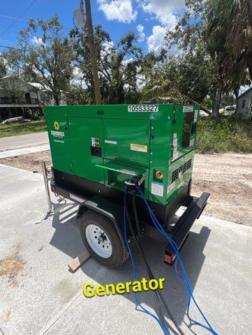 Green generator on a trailer parked outside on a sunny day.