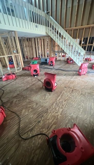 Many red air movers drying out a flooded interior with a staircase.