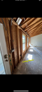 Interior view of a living room under construction, with exposed wooden framing and windows.