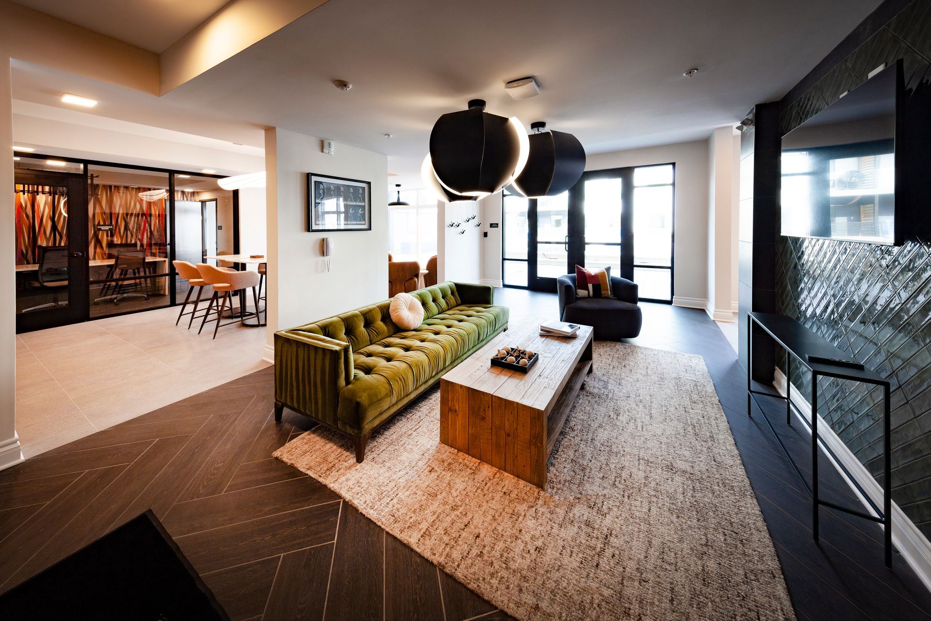 A modern lounge area with a green velvet tufted sofa, a wooden coffee table, a textured rug, and dark accent wall.