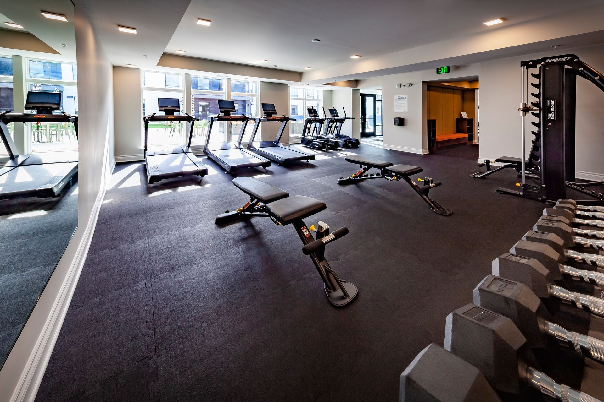 A fitness center with cardio machines, two adjustable weight benches, and a rack of dumbbells on a dark floor.