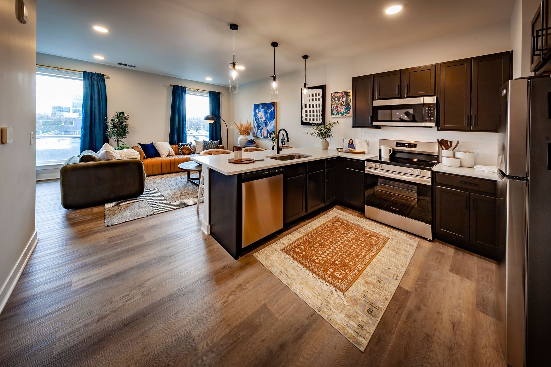 A modern open-concept apartment with a kitchen featuring dark cabinets, stainless steel appliances, and a living area.