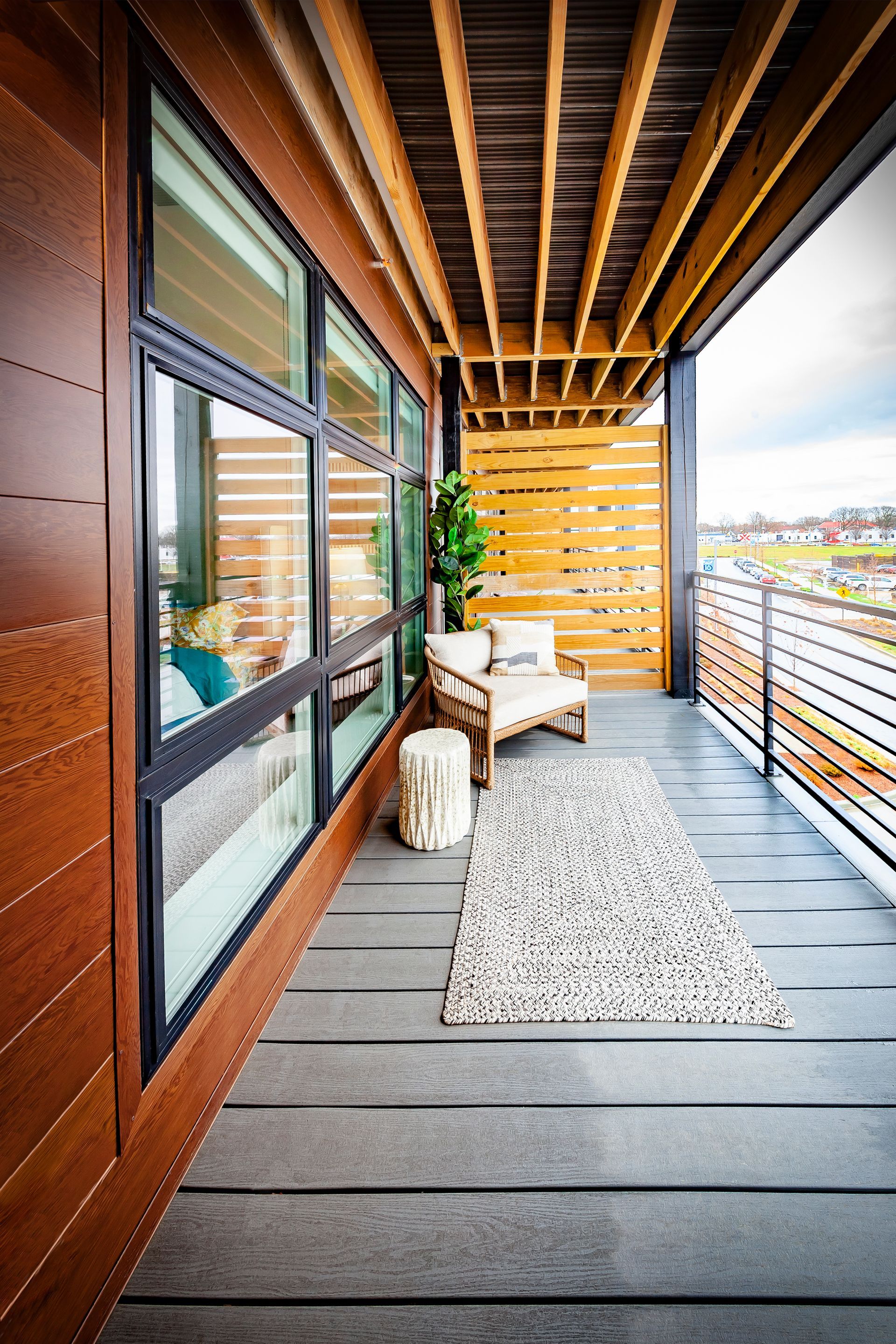 A modern balcony with dark wooden walls, an outdoor chair, a small side table, and a patterned rug on a gray deck.
