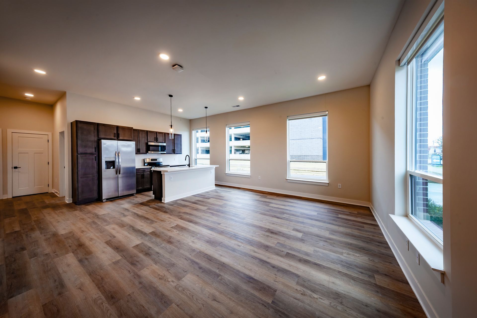 Modern apartment kitchen with wood flooring, dark cabinetry, stainless steel appliances, and a white kitchen island.