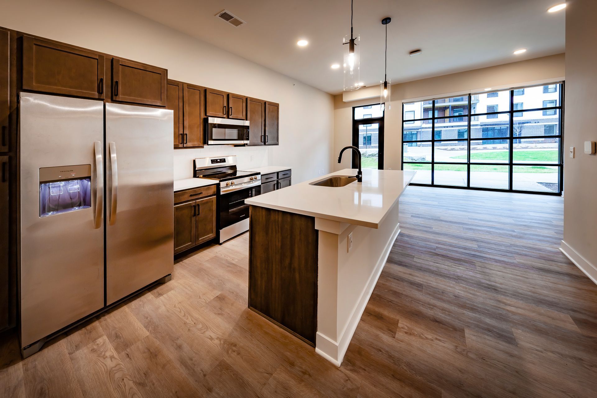 Modern kitchen with wooden cabinets, stainless steel appliances, a white island, and large floor-to-ceiling windows.