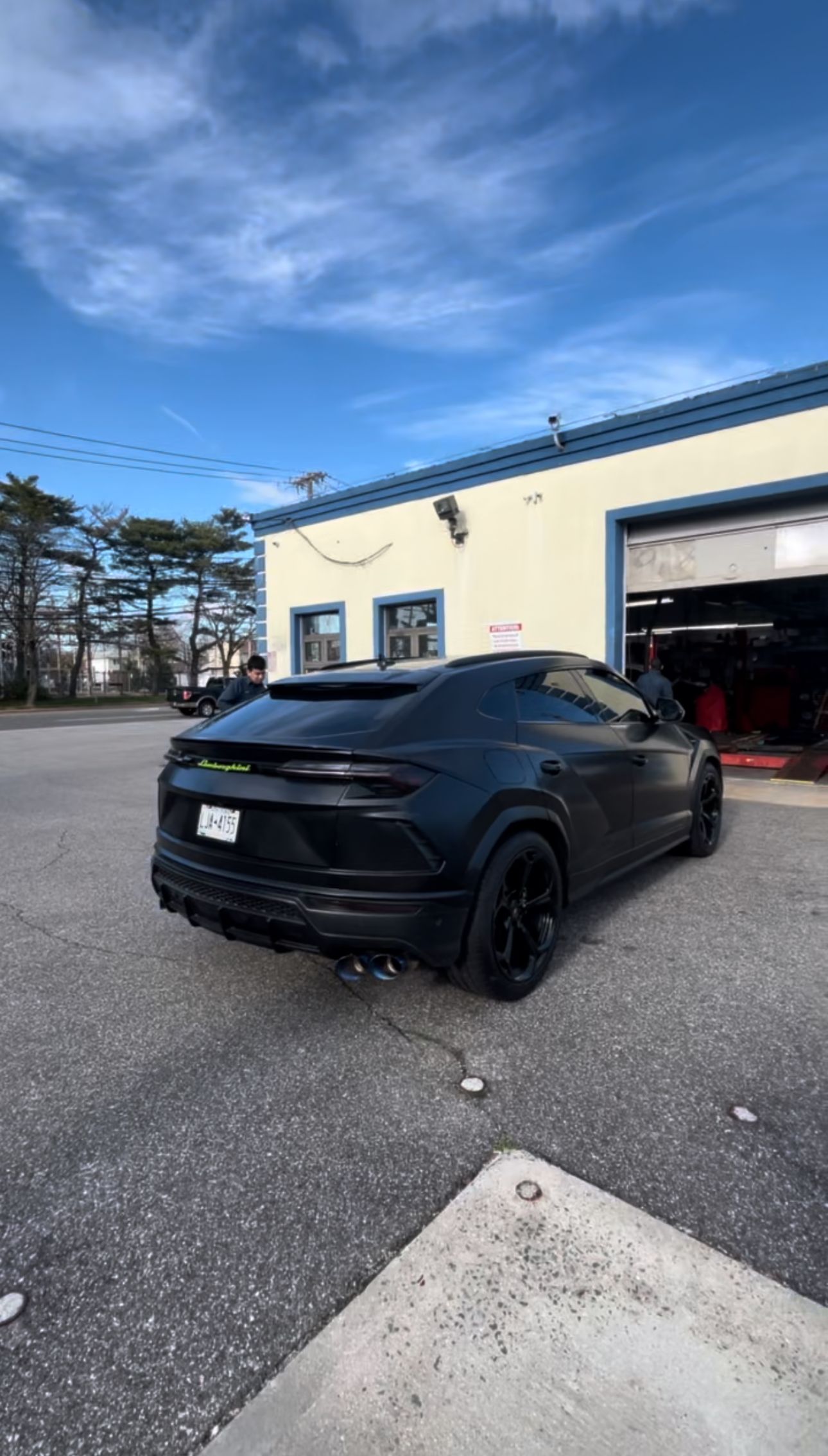 Black Lamborghini Urus SUV parked in front of a building with an open garage door, sunny sky. | Road Ready