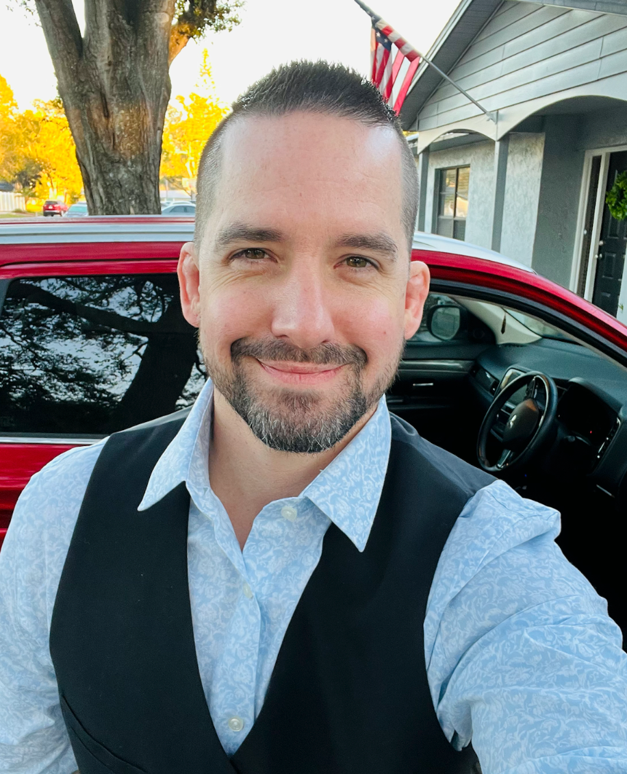 A man is taking a selfie in front of a red car.