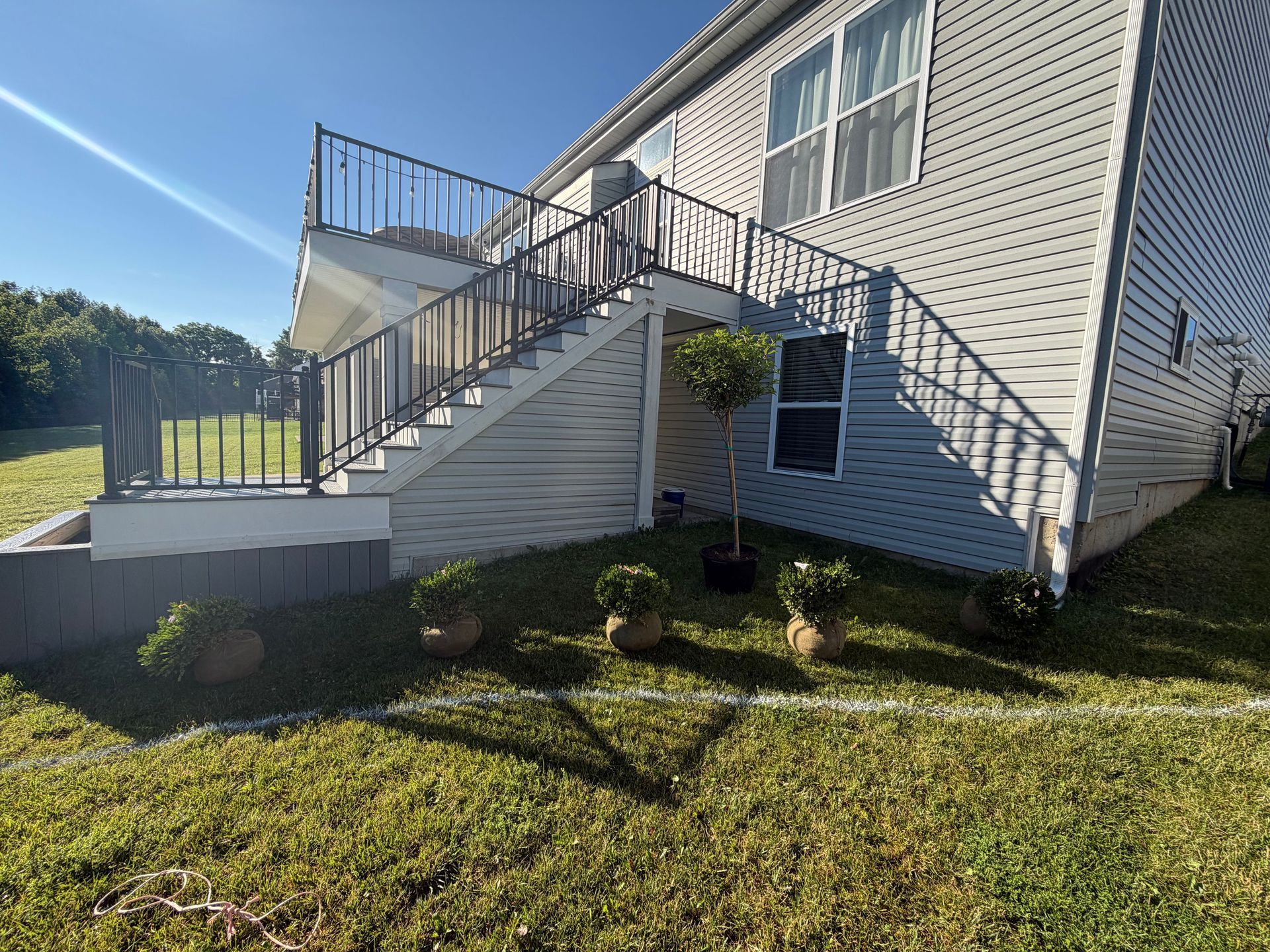 White house exterior with metal staircase and railing, small porch, and grassy yard in sunlight