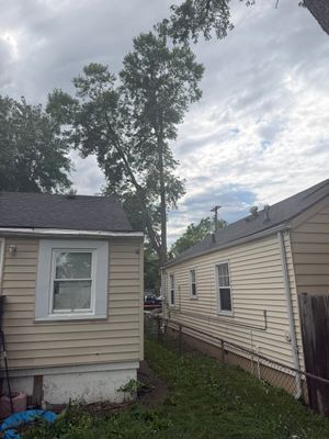 Two beige houses with a narrow grassy gap between them and a tall tree under a cloudy sky.
