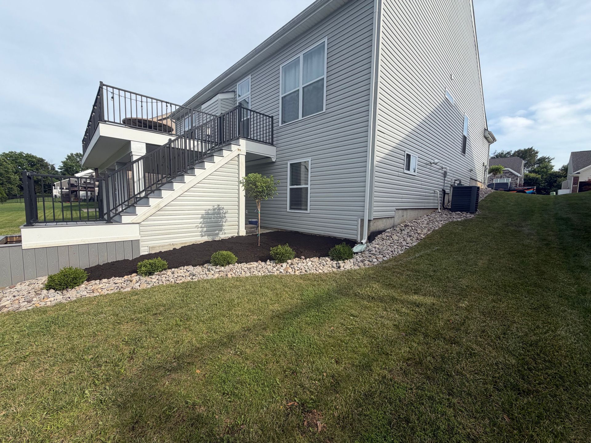 Exterior of a white two-story house with a deck, stairs, and grassy yard on a sunny day