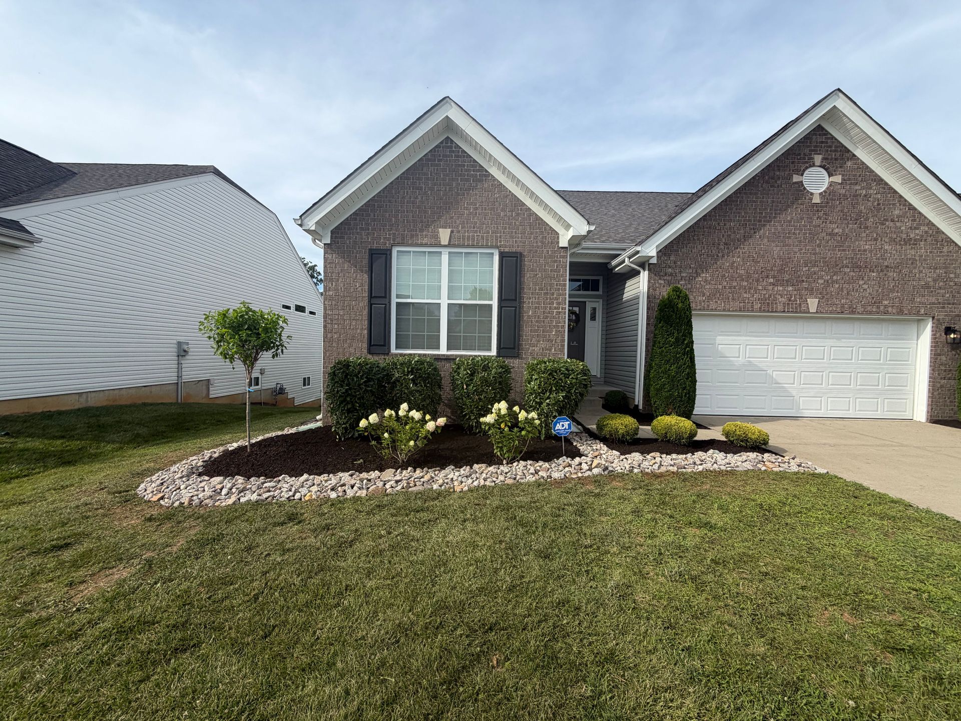 Single-story brick house with a two-car garage, white trim, and a landscaped front yard.