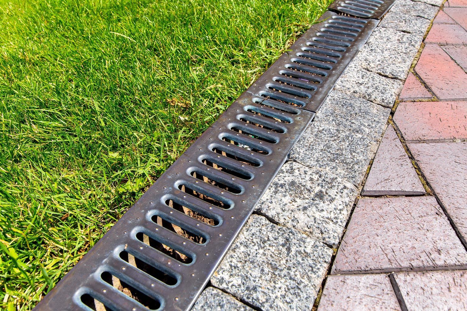 Drain grate along a grassy edge beside a brick sidewalk Drain grate along a grassy edge beside a brick sidewalk