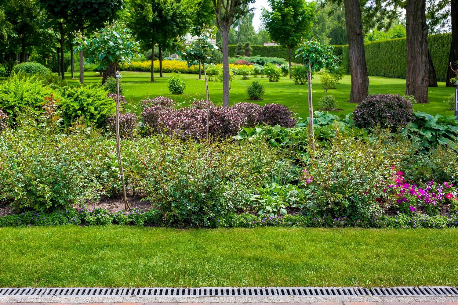 Lush green park garden with colorful flower beds, trees, and a grassy lawn bordered by a path