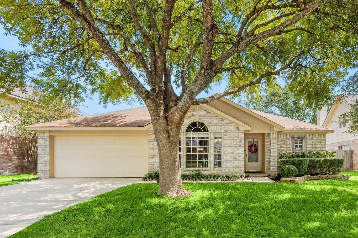 Suburban single-story house with a large front tree, green lawn, and two-car garage Suburban single-story house with a large front tree, green lawn, and two-car garage