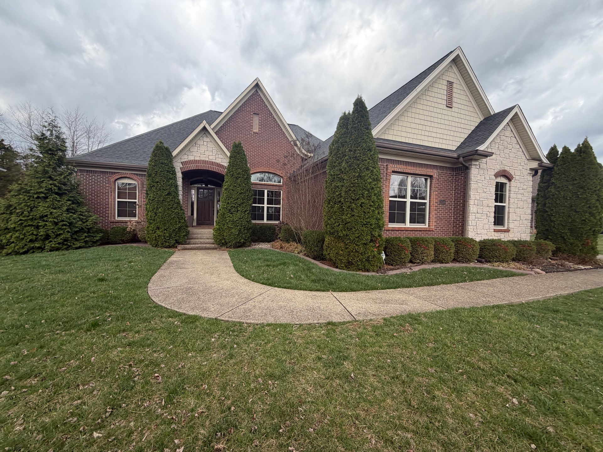 Brick house with peaked roofs, arched entry, and a curved walkway across a green front lawn
