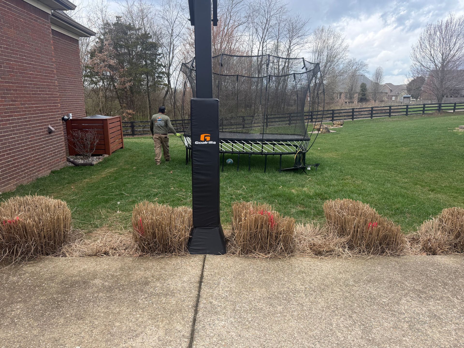 Backyard patio with a black lamp post, brick house, shrubs, and a green bench in the background.