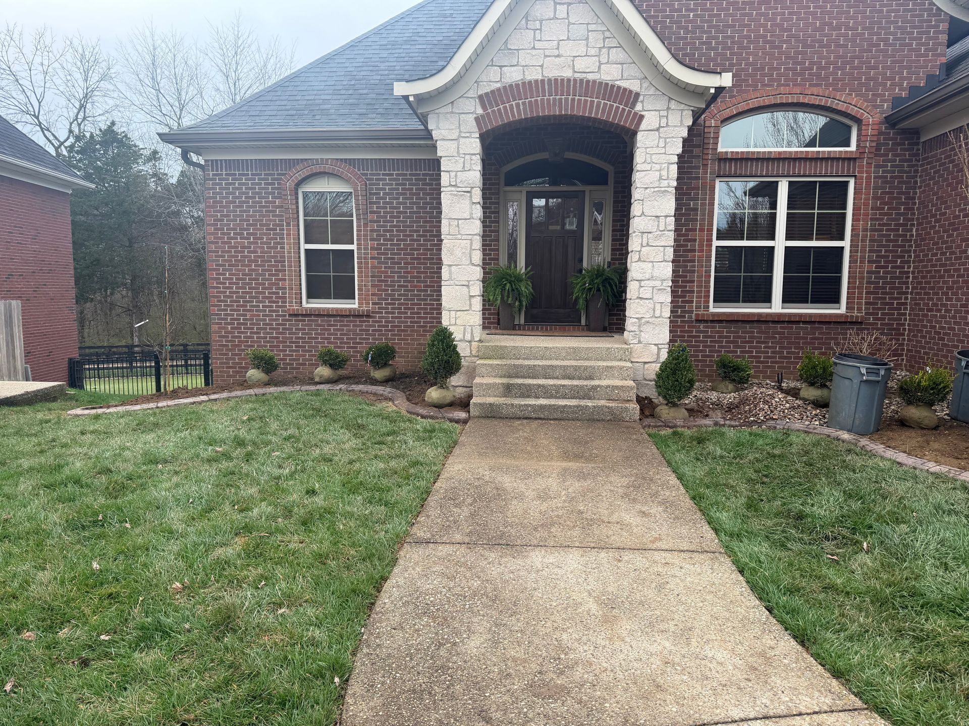 Brick house front entrance with arched porch, concrete walkway, and small landscaped lawn