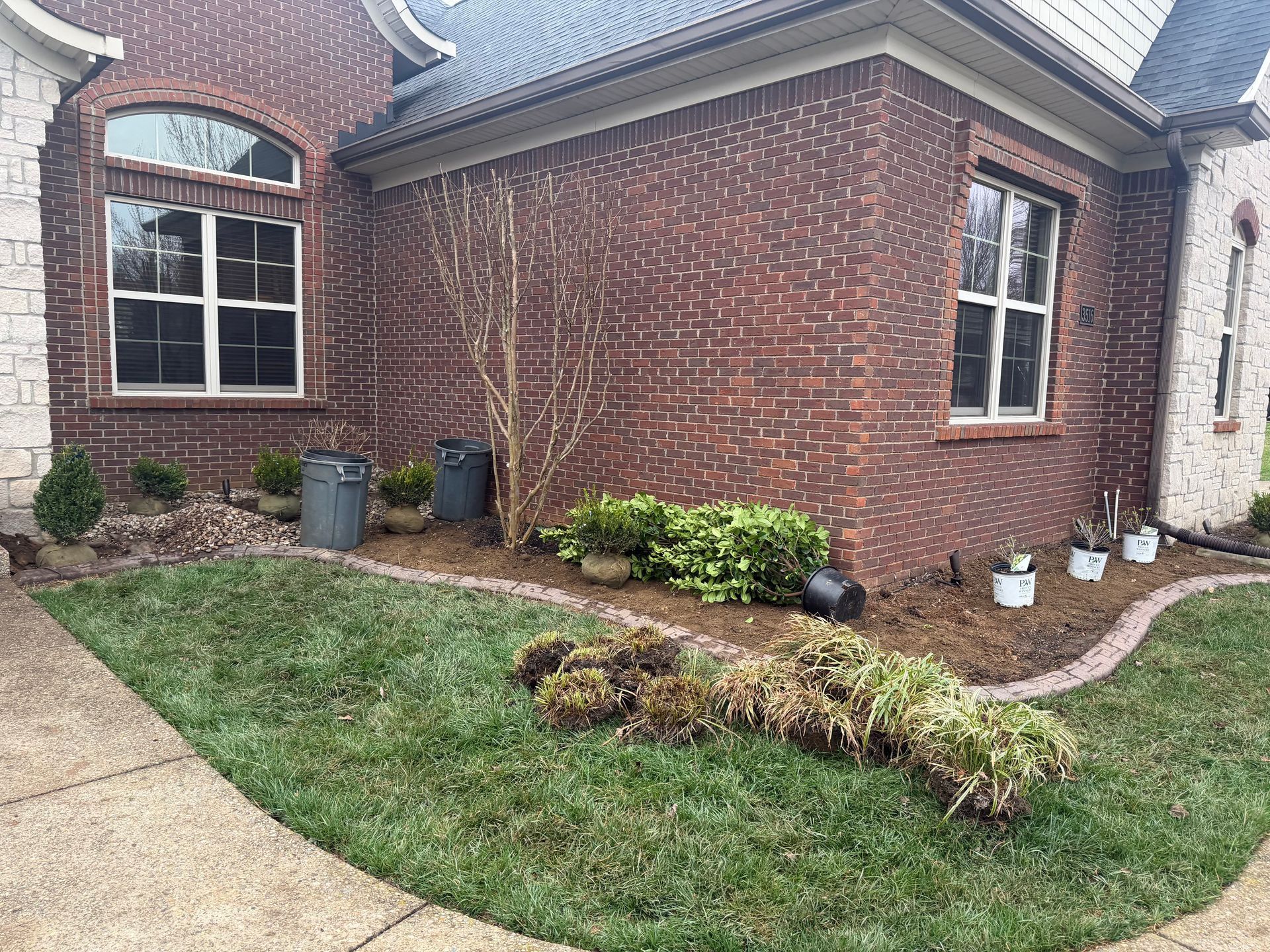 Brick house corner with arched windows, curved walkway, and landscaped grass and shrubs.