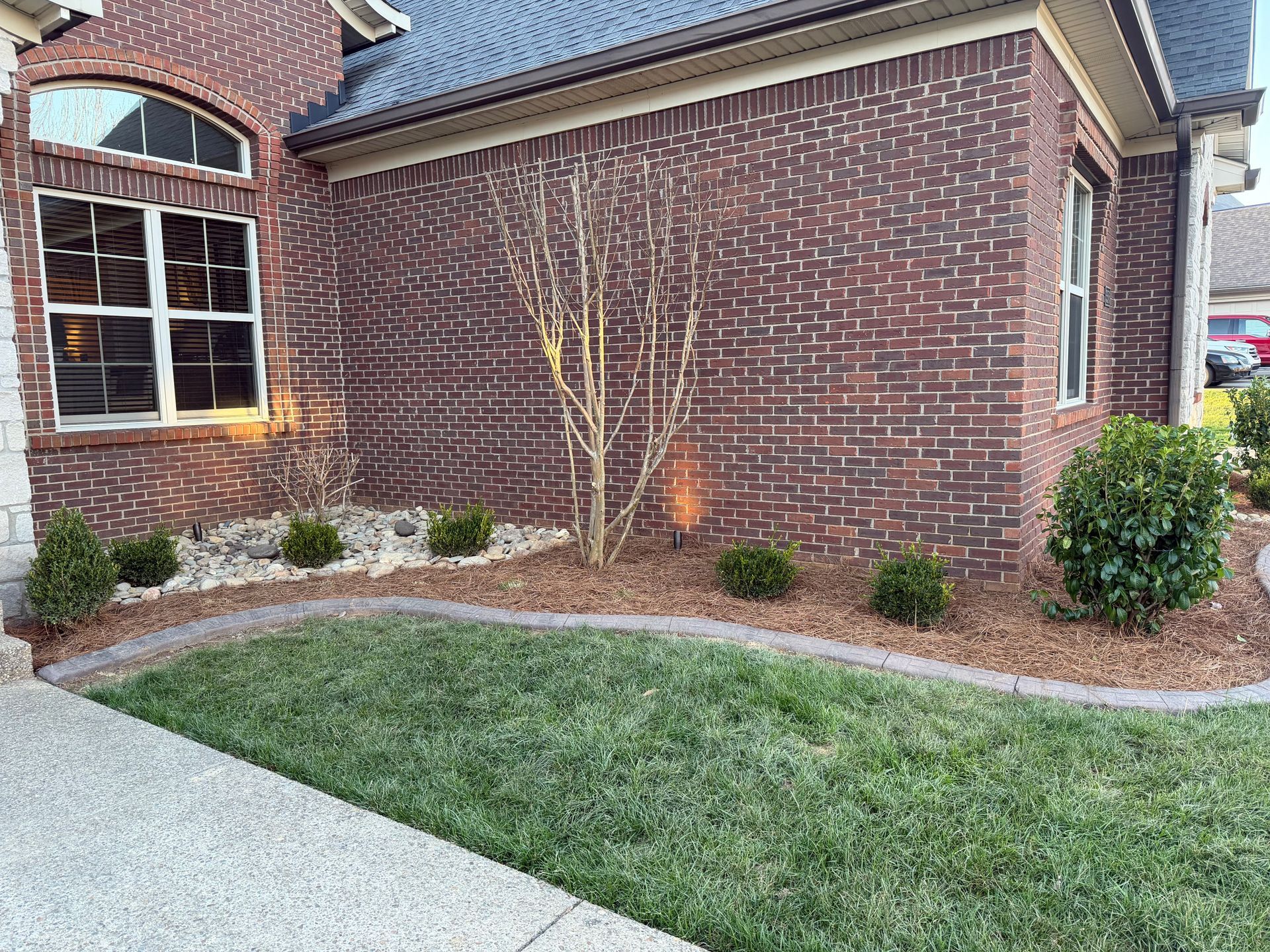 Brick house exterior with small landscaped garden, lawn, and concrete driveway