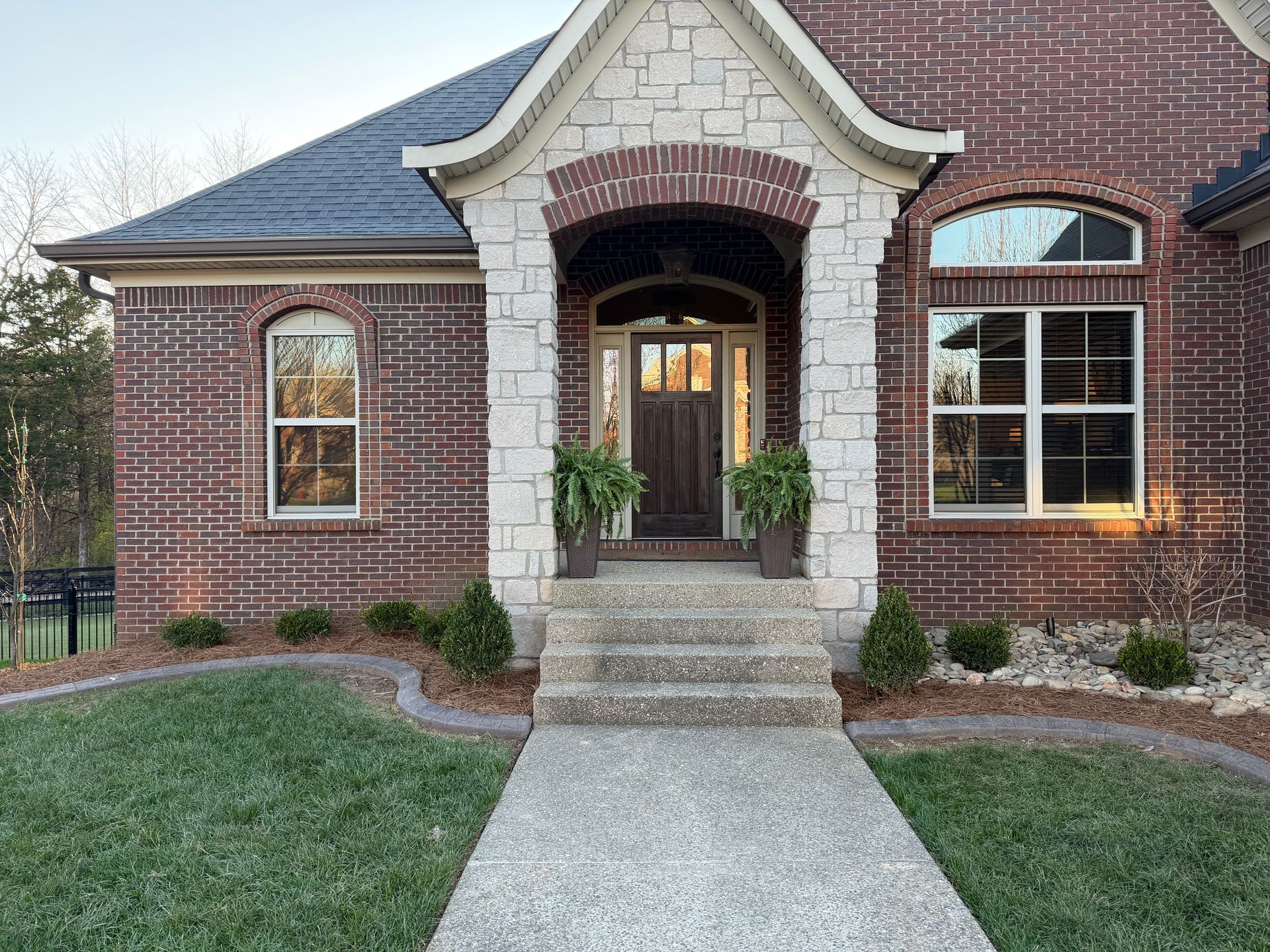 Brick house front entrance with arched porch, white columns, and a concrete walkway leading to the door