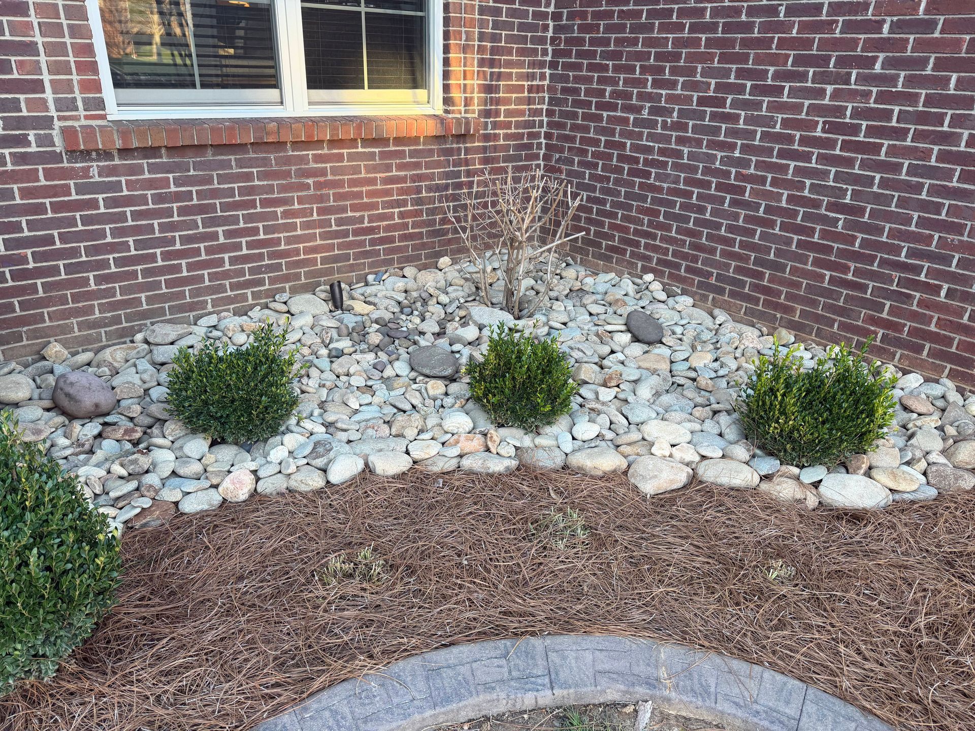Brick house exterior with a landscaped stone bed, small shrubs, and a curved mulch border.