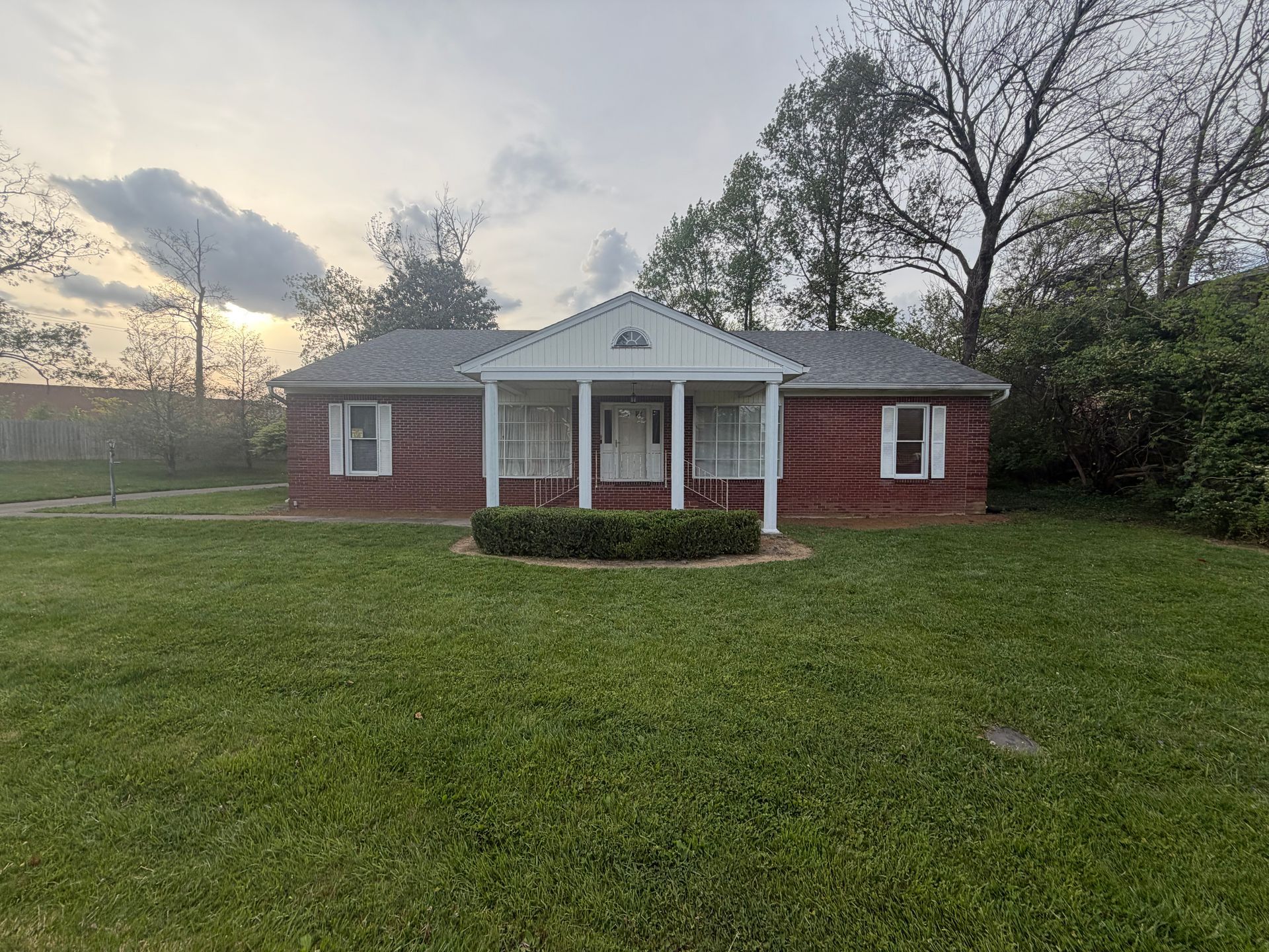 Small brick house with white columns and a wide green lawn at sunset