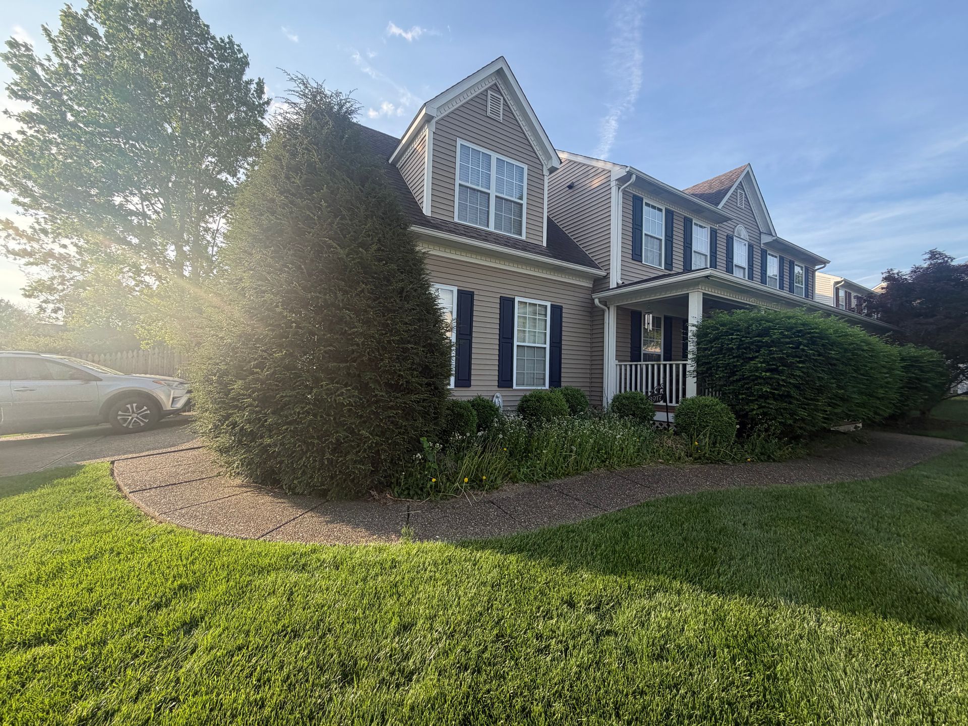 Two-story suburban house with stone facade, blue shutters, and a sunlit front lawn