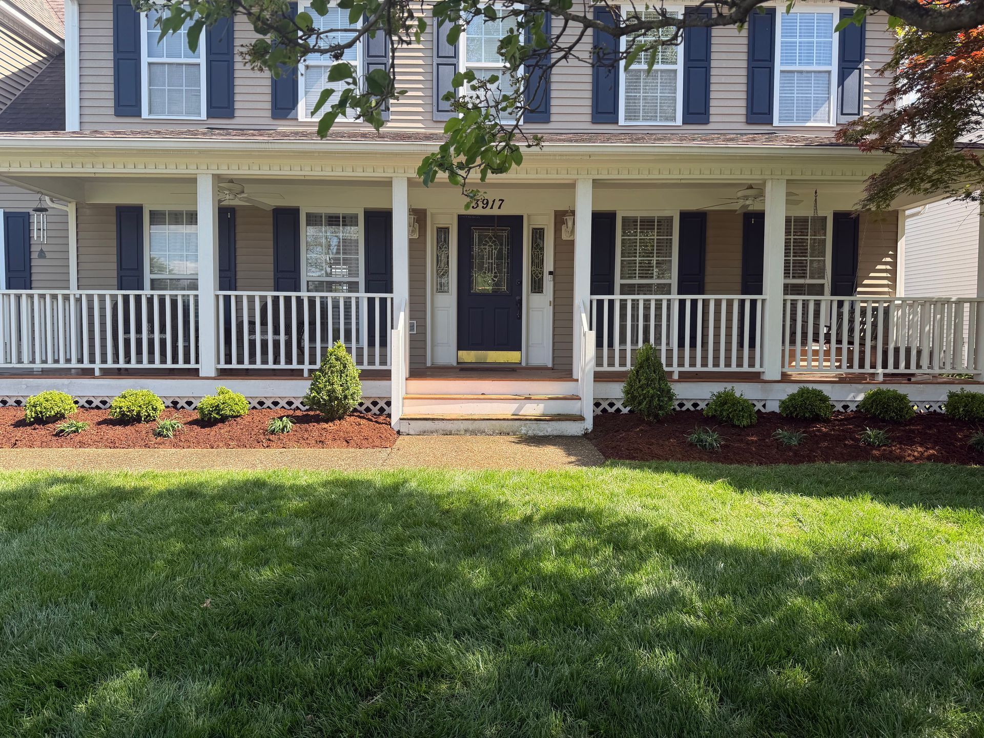 Two-story house with a front porch, white railings, blue shutters, and a green lawn