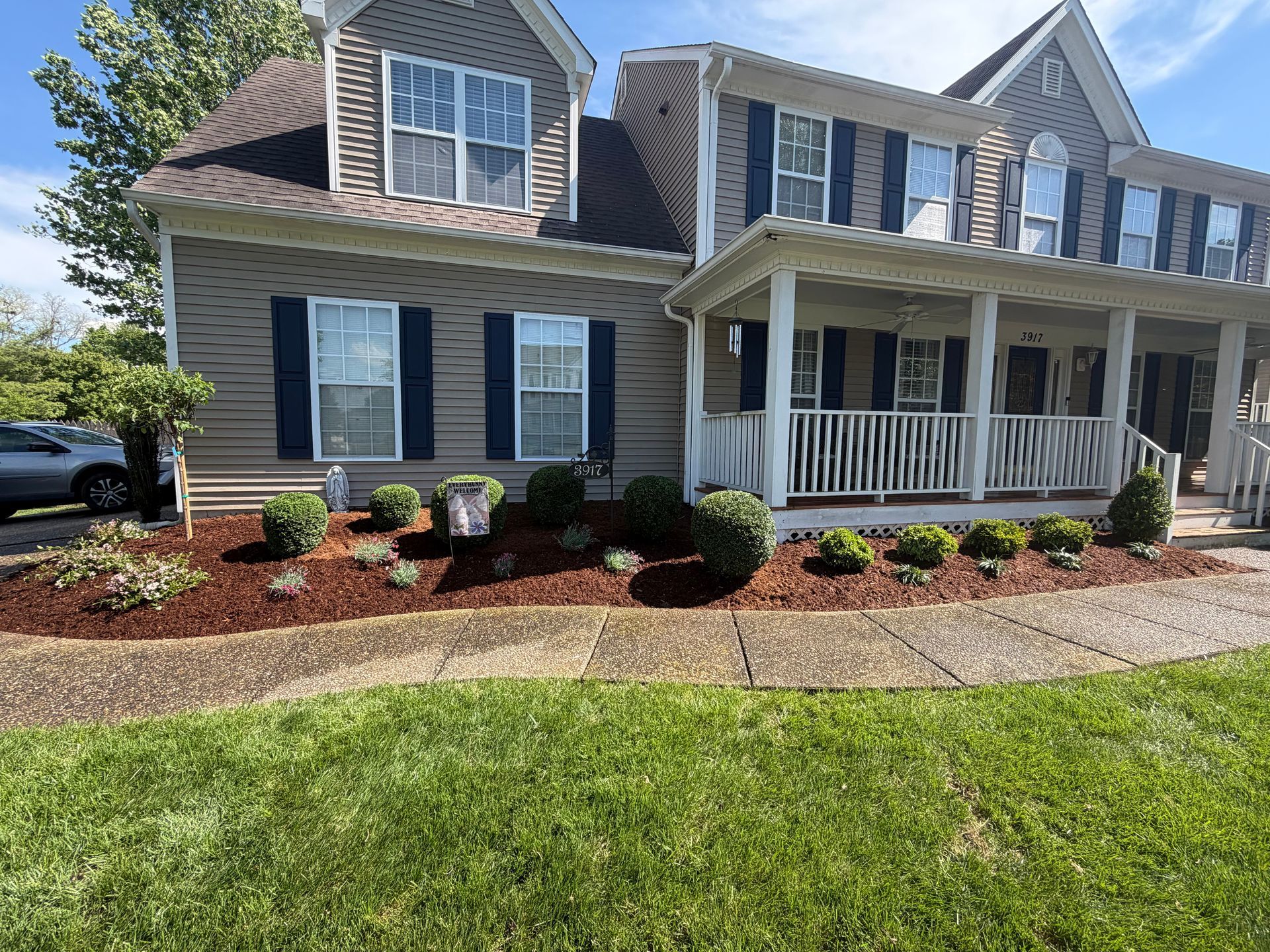 Suburban house with gray siding, white porch, black shutters, and a manicured lawn in front.