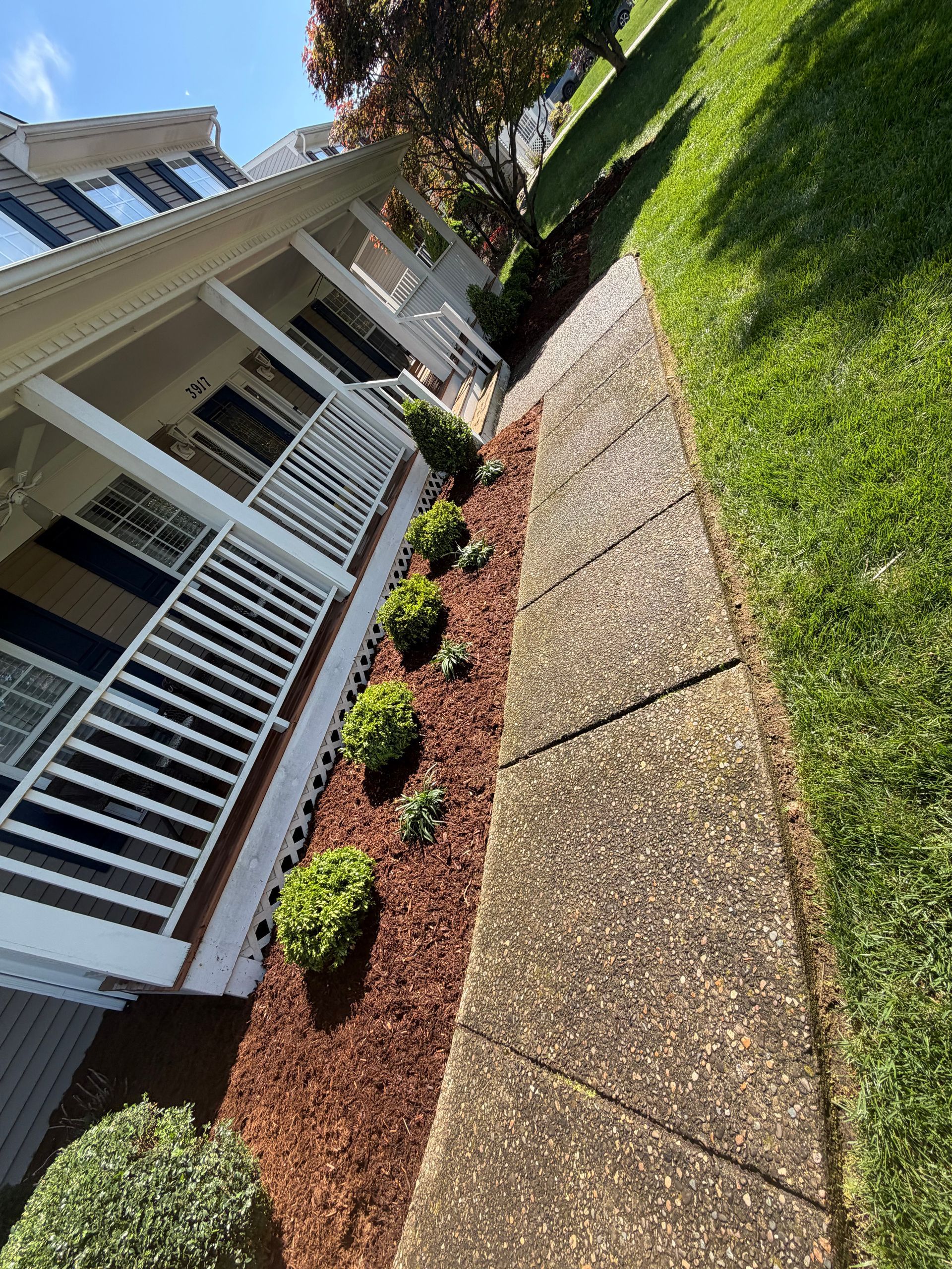 Front yard with white house porch, curved stone walkway, and green lawn with mulched flower bed.