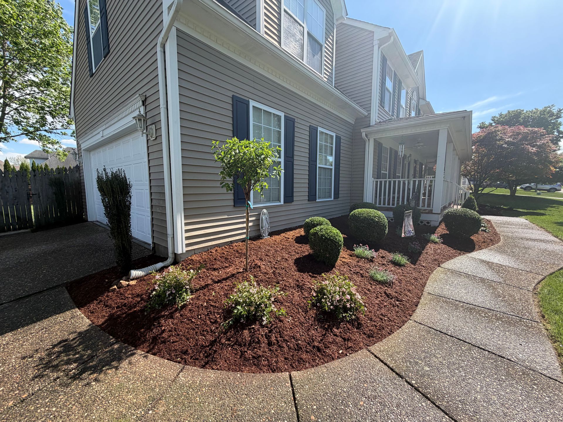 Suburban house exterior with landscaped front yard, curved walkway, and bright sunlight.