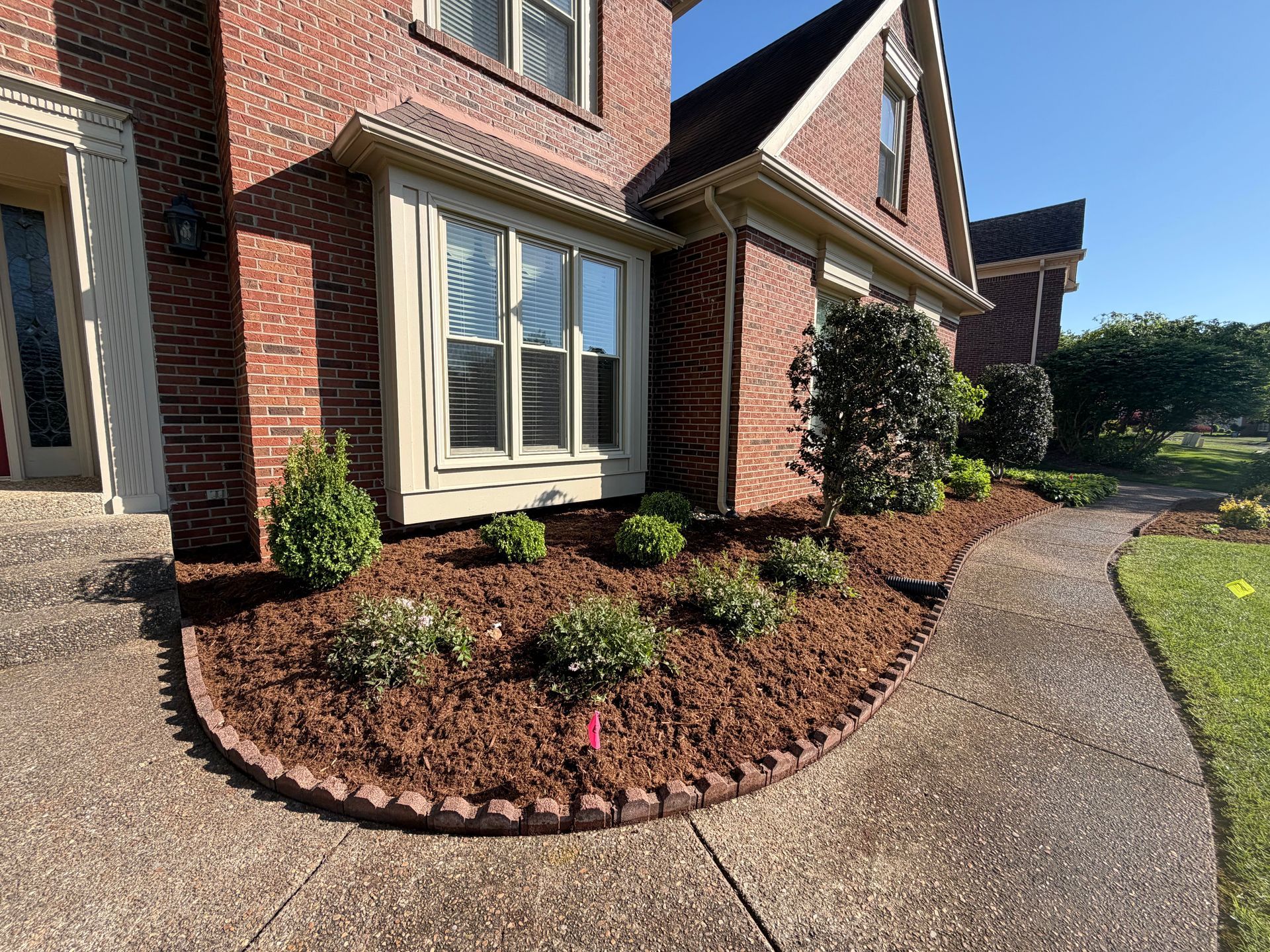Brick house front with curved concrete walkway and landscaped mulch beds